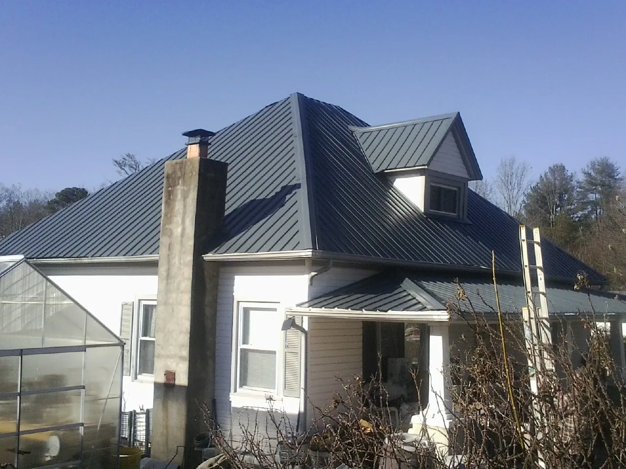 Dark blue standing seam metal roof on a white farmhouse with dormer — Slate & Tile Roof Repair by Roofing Brothers in Peachland