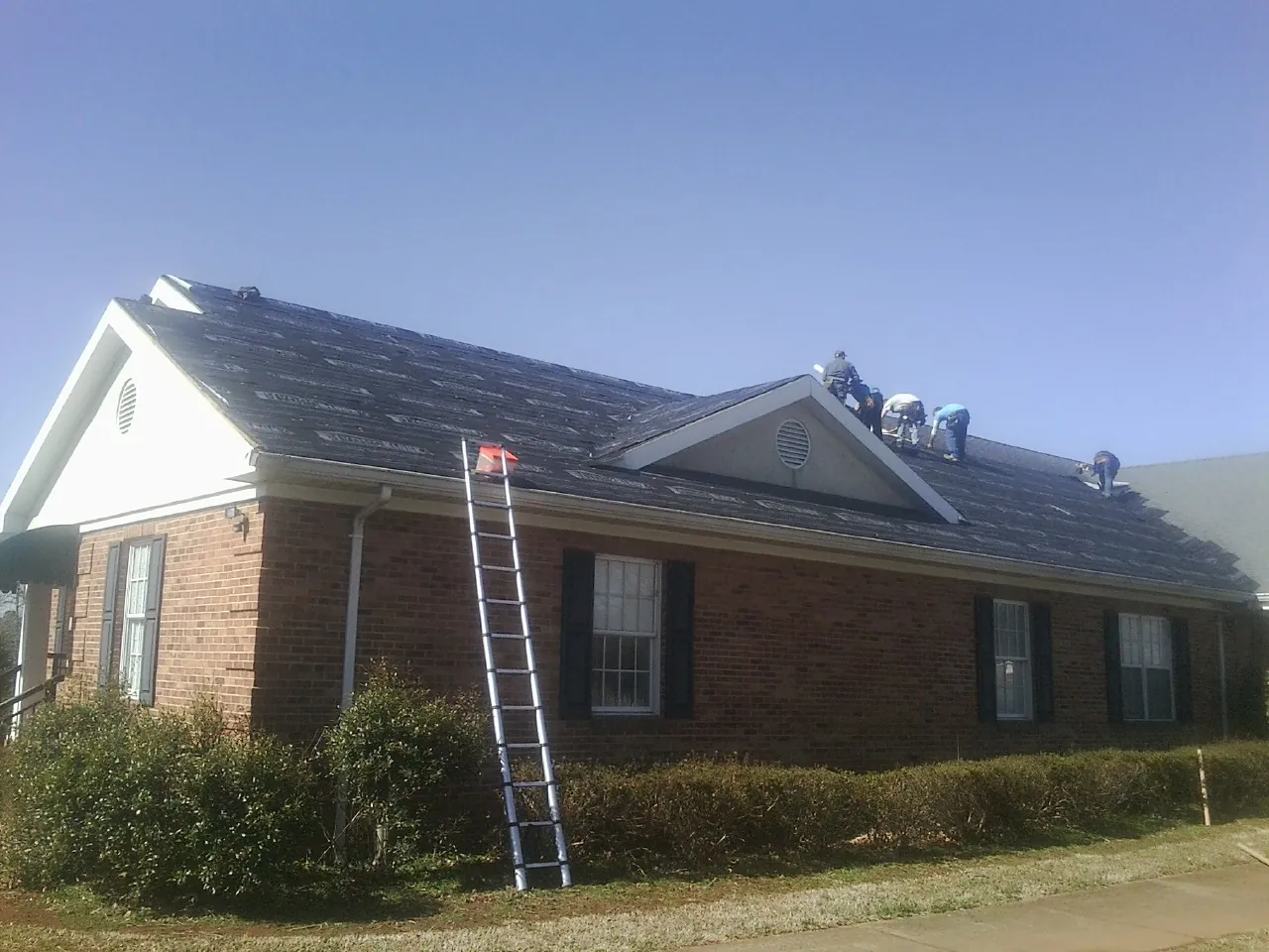 Crew tearing shingles off a brick ranch roof with a ladder set — Emergency Roof Repair work by our crew in Peachland