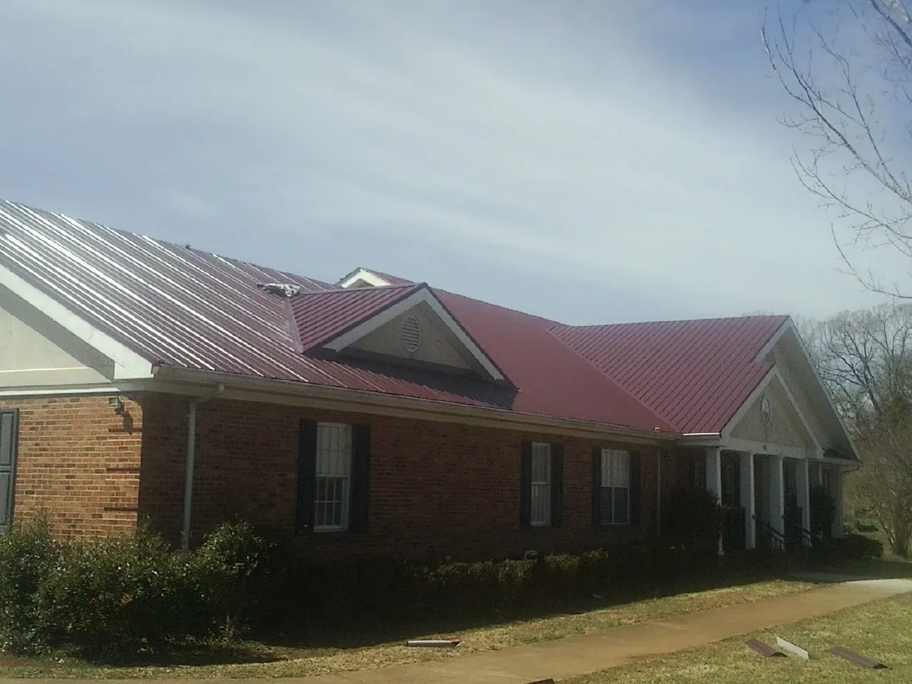 Red metal roof with gabled entries on a long brick building, from a Hail Damage Roof Repair job in Peachland