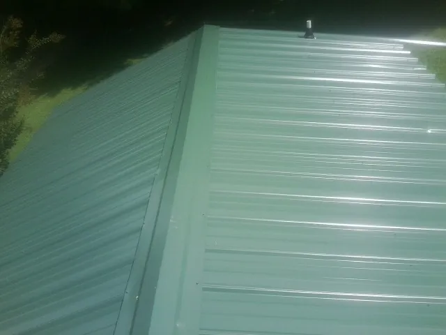 New green metal panels meeting at the ridge of a roof — Flat Roof Repair work by our crew in Peachland