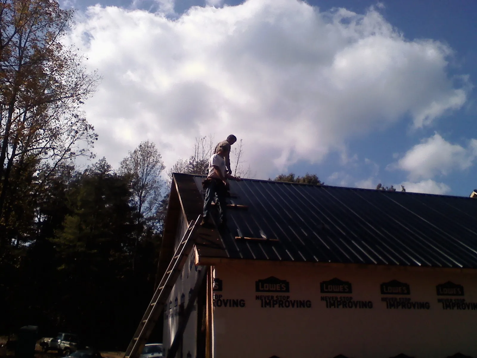 Roofer fastening dark metal panels high against a cloudy sky, from a Roof Inspection job in Peachland