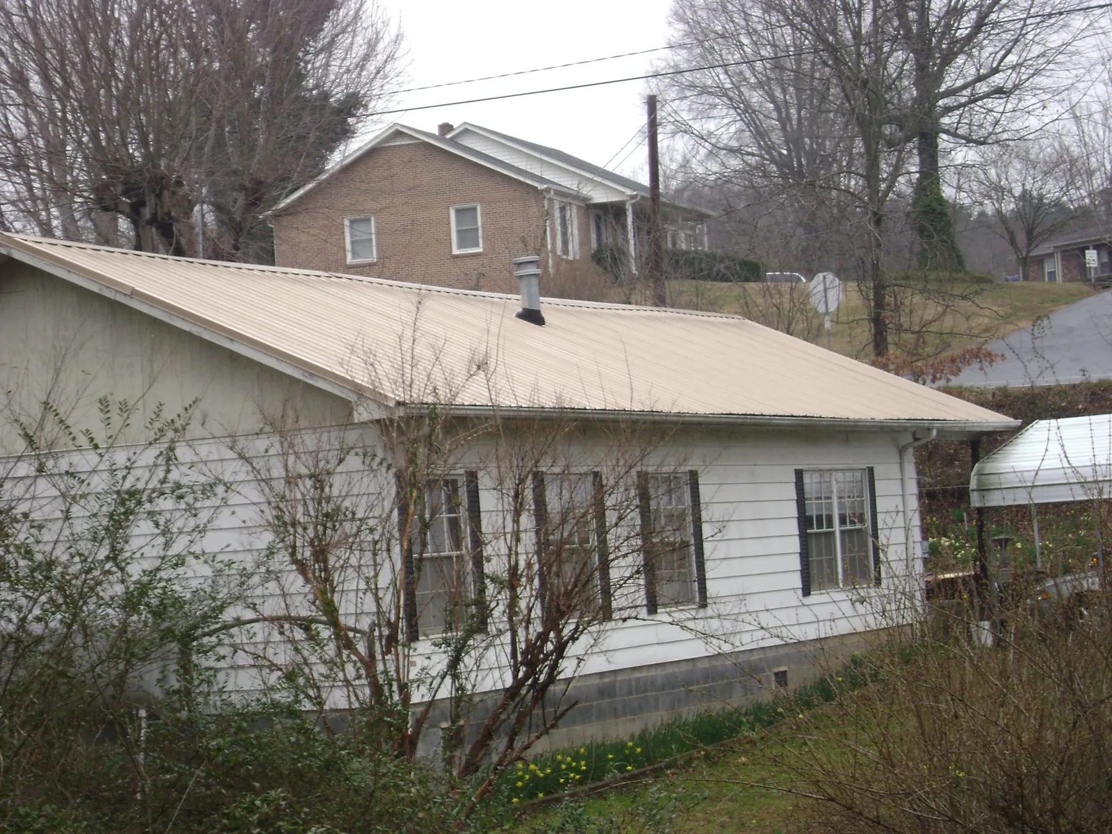 Tan metal roof on a white sided house set into a hillside — Commercial Roofing by Roofing Brothers in Peachland